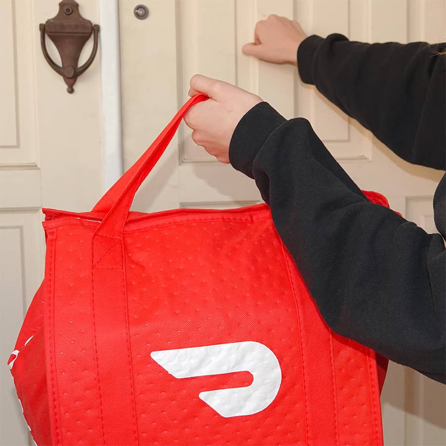 delivery person with door dash bag knocking on a white front door